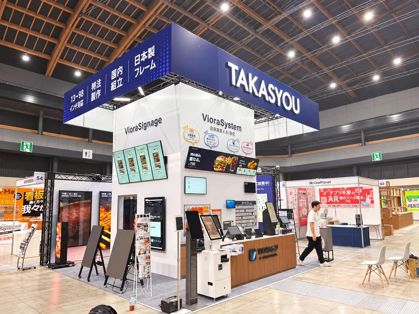 展示会での高昇ブースの写真。TAKASYOUの看板の下に、マルチディスプレイ、メニューボード、LEDスタンド、セルフオーダー端末やPOSレジが並んでいます。